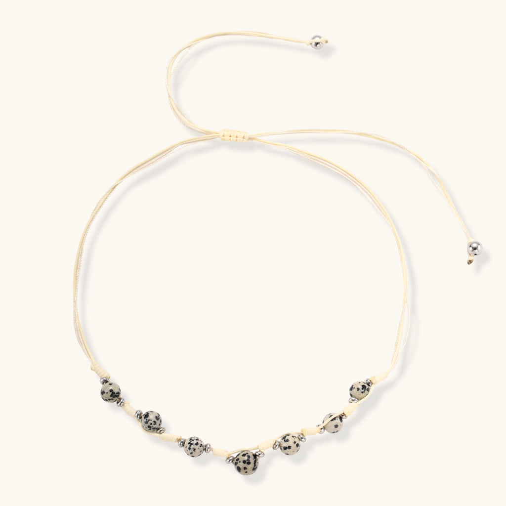 Adjustable cream cord necklace with white spotted stone beads featuring black speckles on neutral background