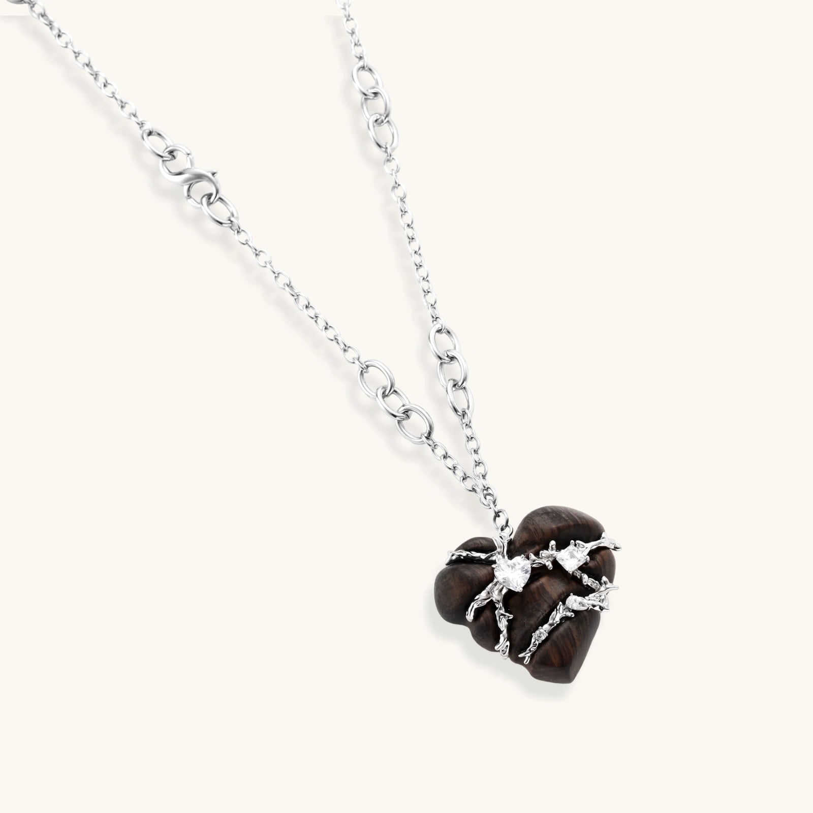 Dark ebony wood heart pendant wrapped with brass wire and zirconia crystals on adjustable chain against cream background